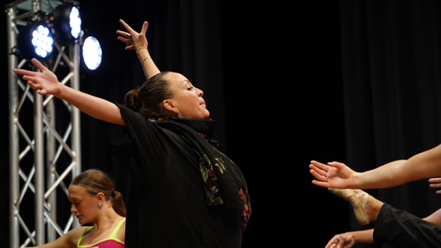 Dancer with arms extended on stage under bright light